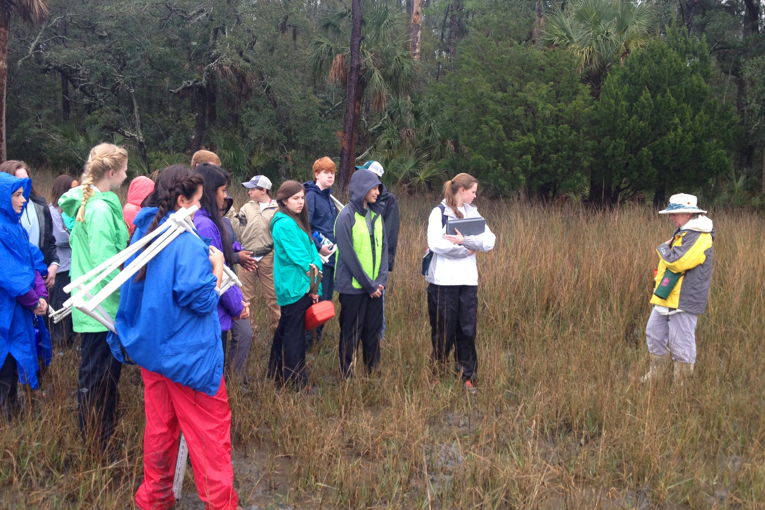 a group of teenagers wearing jackets stand in a marsh