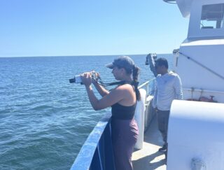 a woman stands on the deck of a vessel on the ocean while looking through an instrument