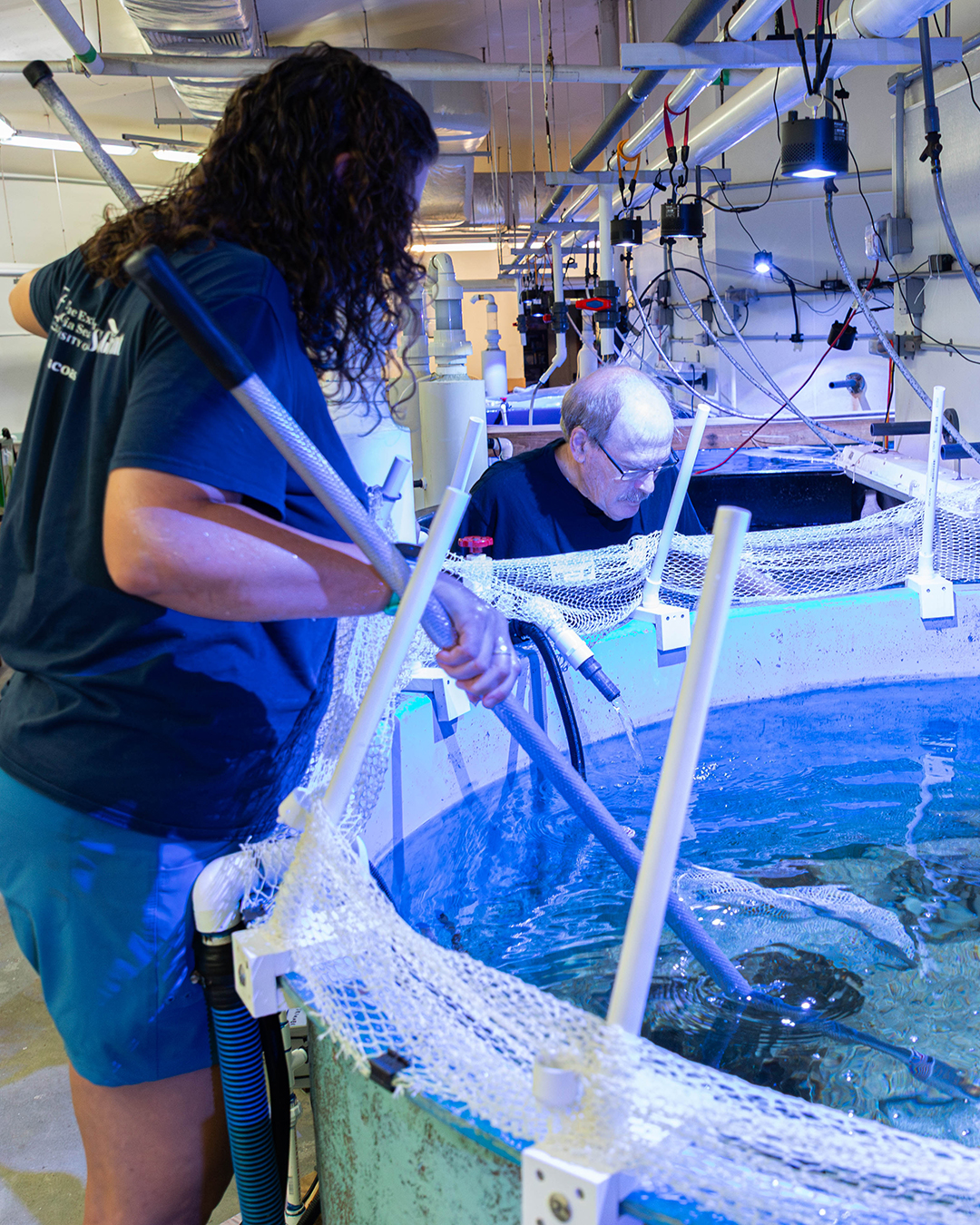 Two people are working with a large circular water tank in an aquarium.