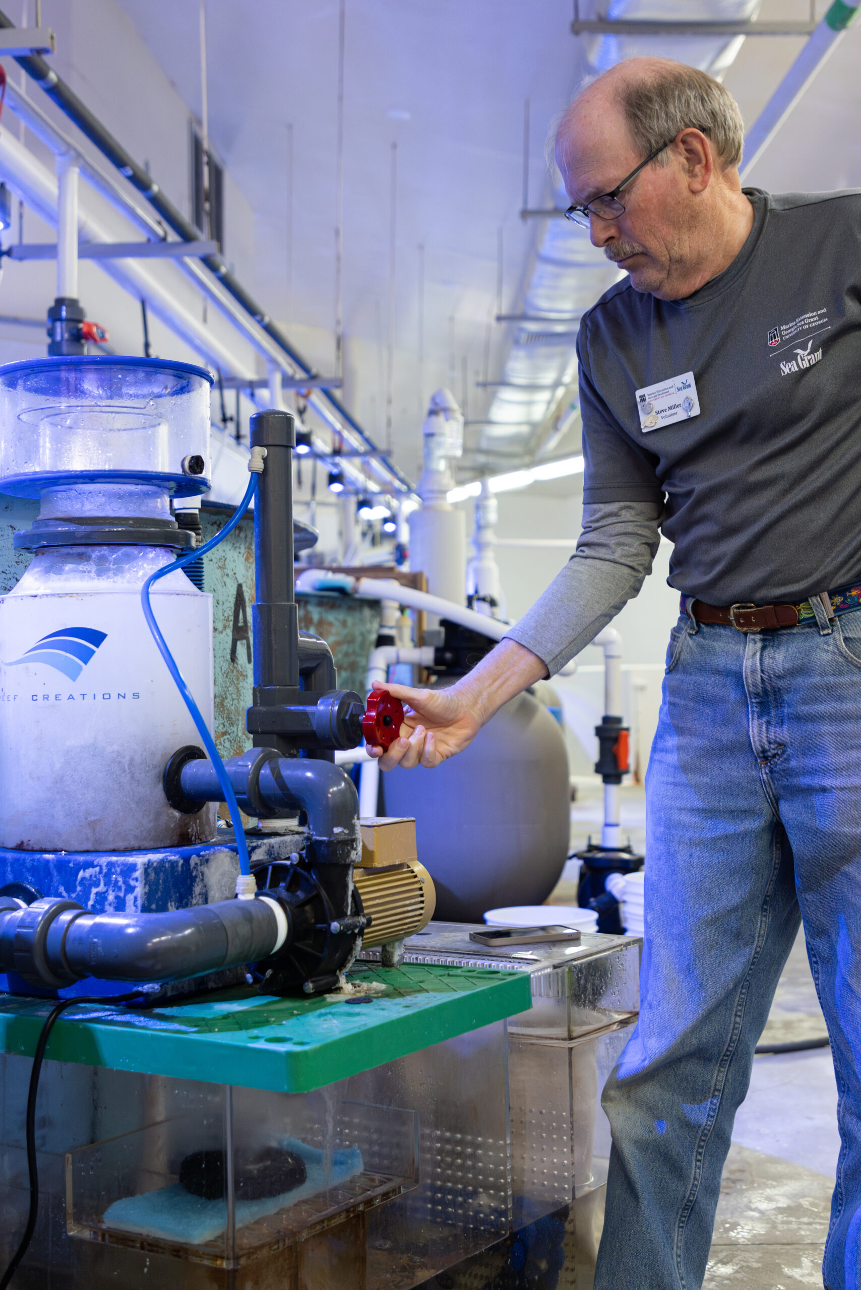 A man adjusts a valve on equipment near tanks at an aquarium.