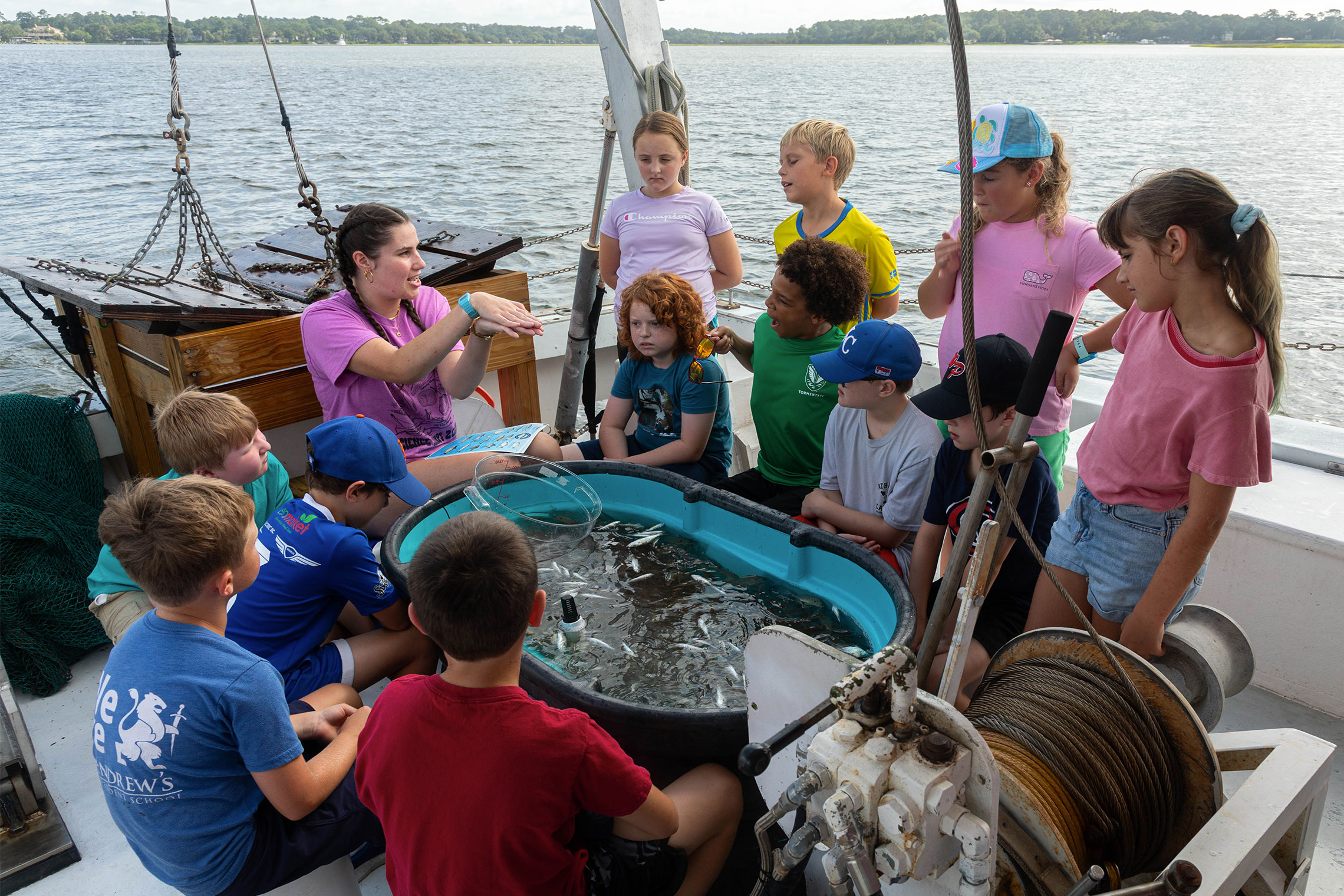 An instructor on a boat shows a group of children a tub filled with small fish caught during a trawl
