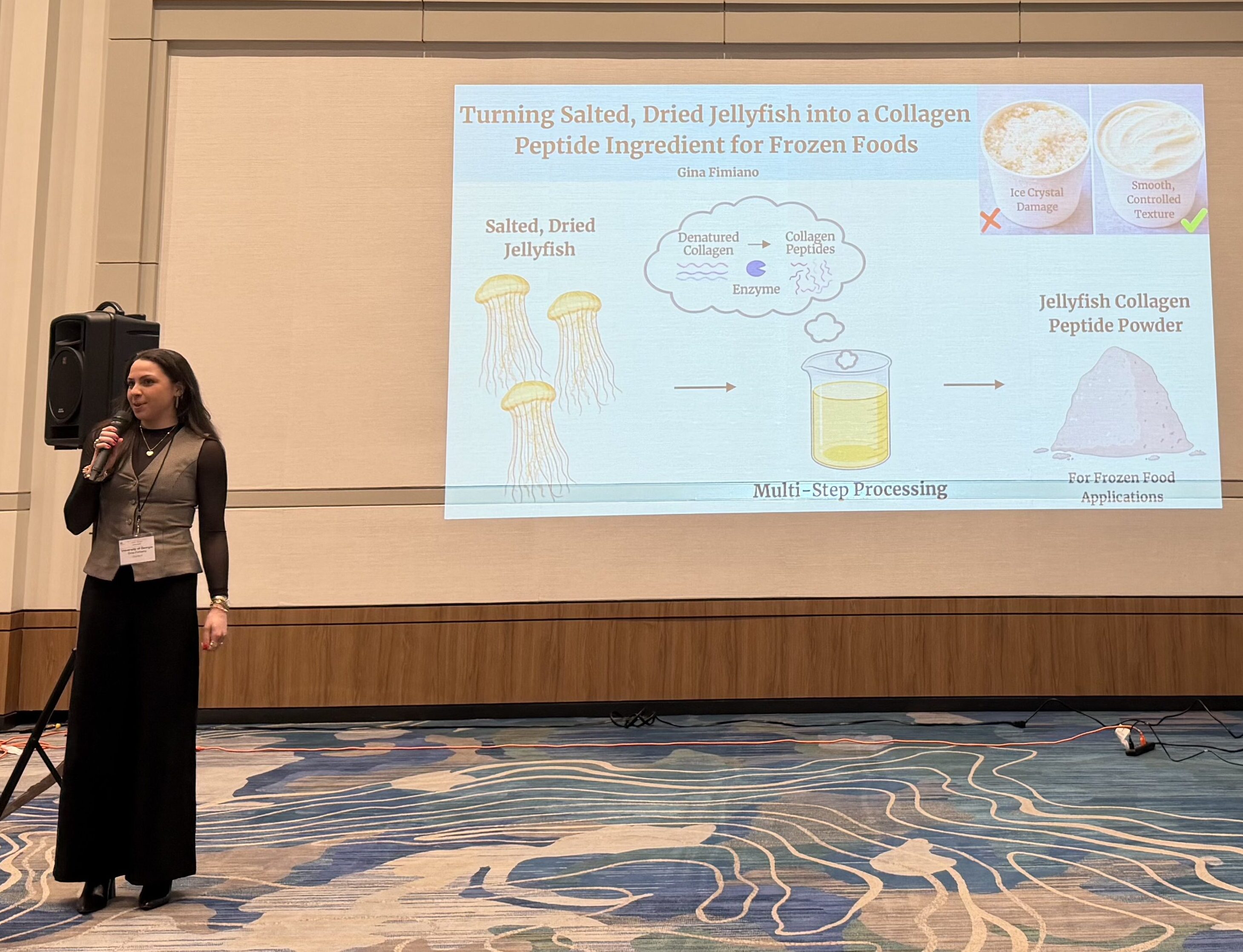 Gina Fimiano holds a microphone while standing in front of a projected presentation titled Turning Salted, Dried Jellyfish into a collagen peptide ingredient for frozen foods