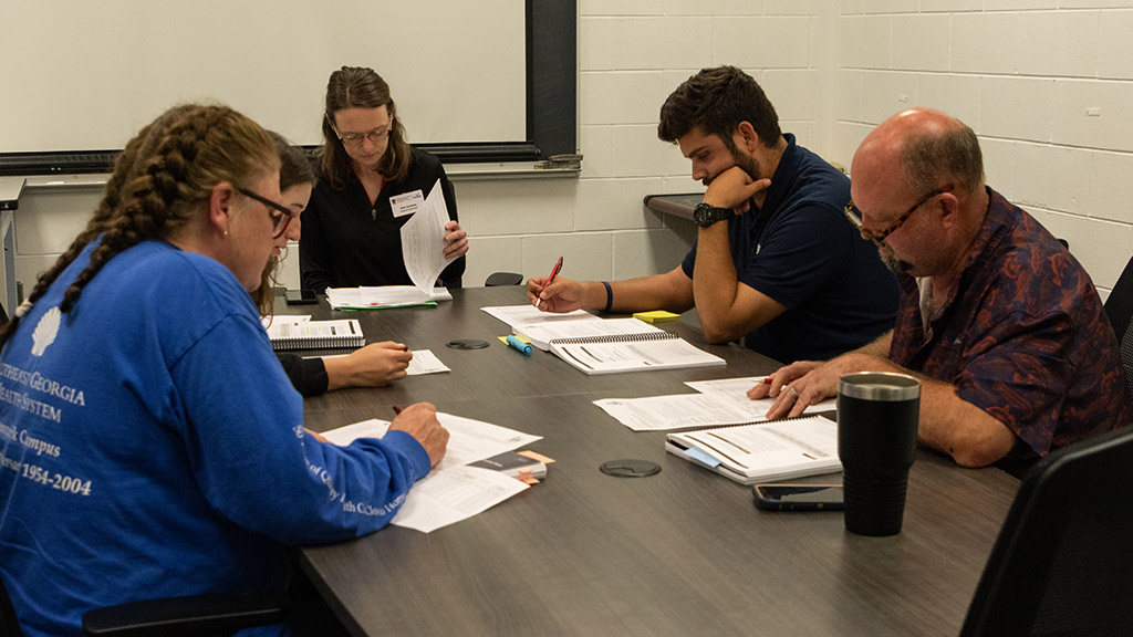 five people sit around a conference table looking at papers