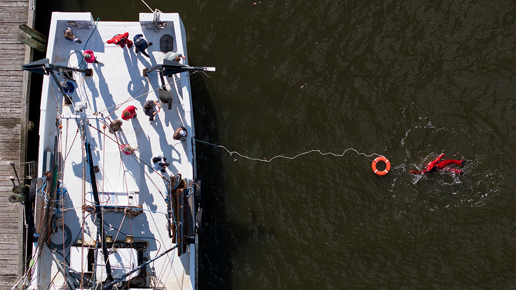 aerial view of a fishing vessel with a training instructor swimming towards a lifesaver in the water