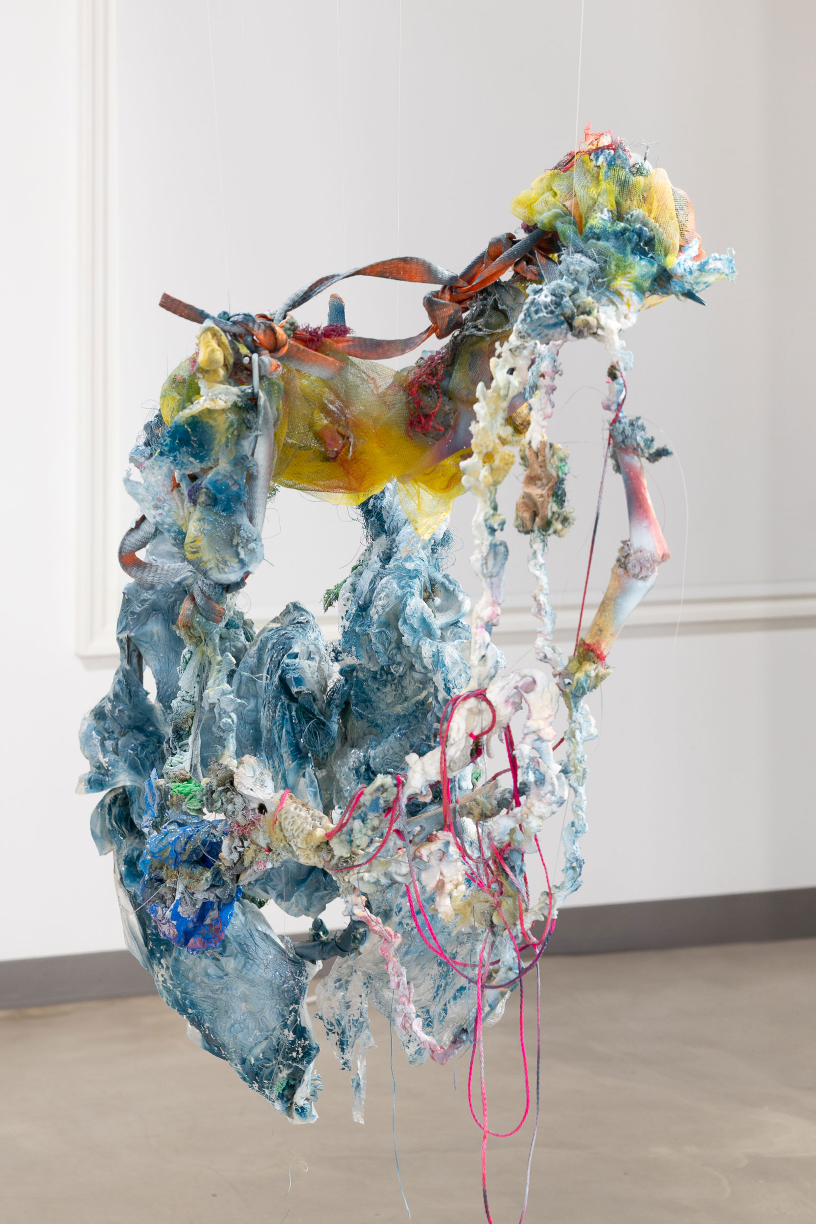 an abstract art piece made from light blue reclaimed materials hangs mid air in a gallery space