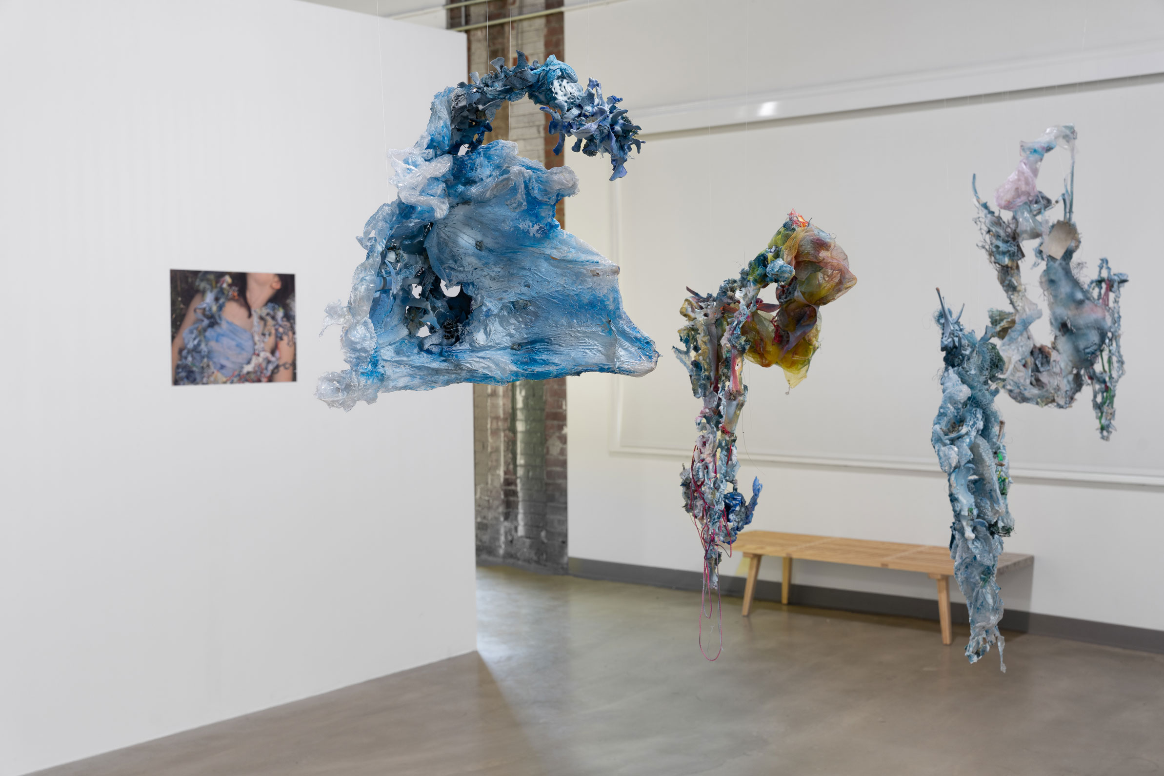 an abstract art piece in the shape of a wave made from light blue reclaimed materials hangs mid air in a gallery space