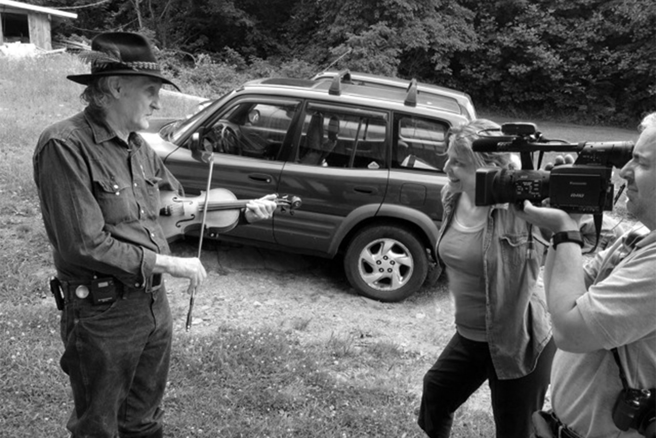 outside, a man plays a violin while a video camera films