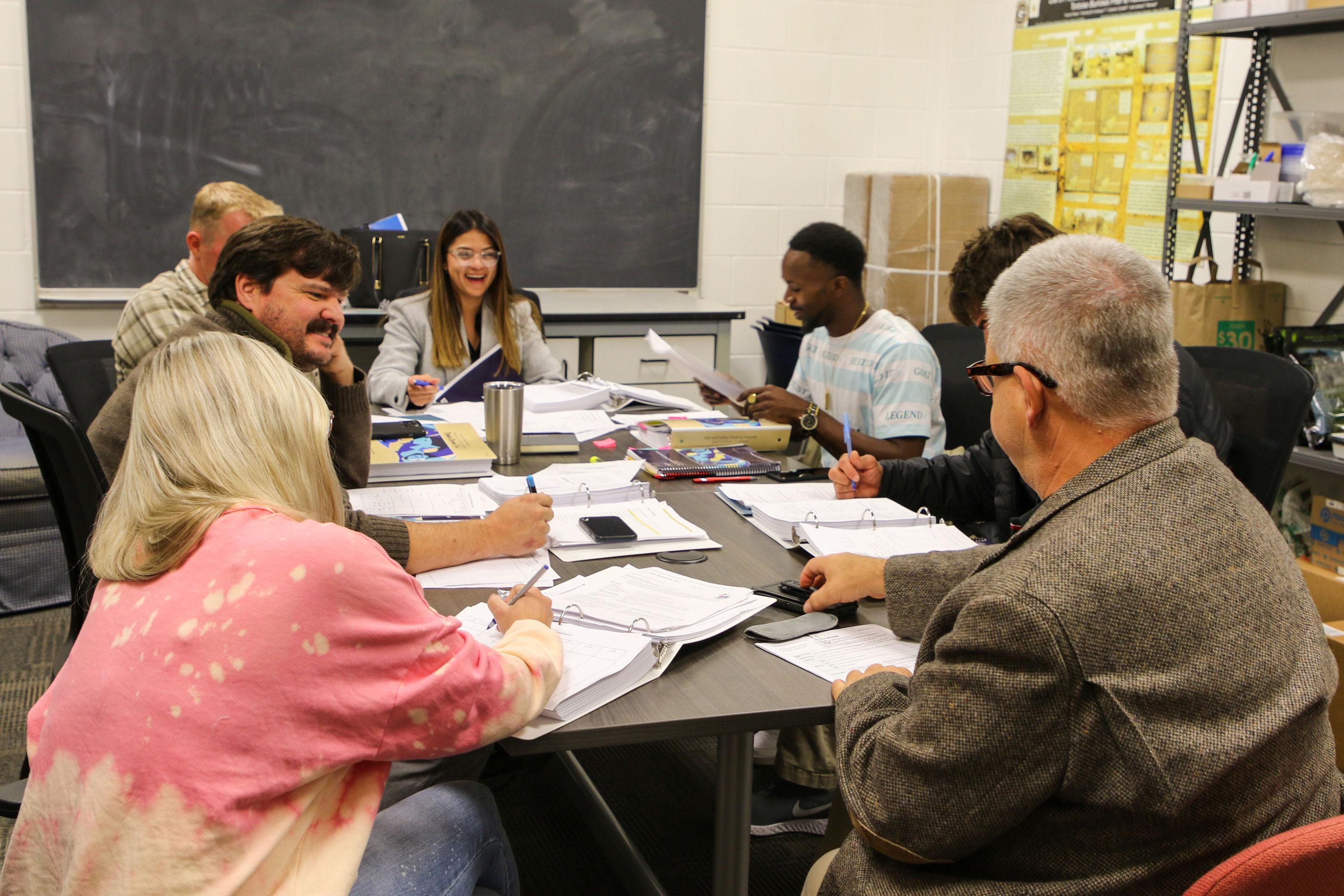 a group of adults sit in a conference room around a table in discussion