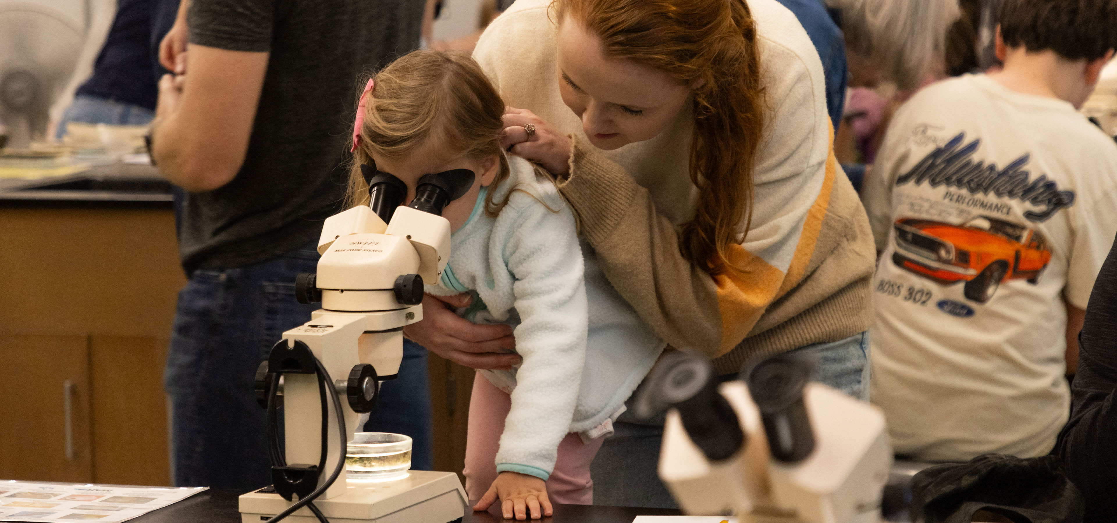 a woman assists a young girl in looking through a microscope