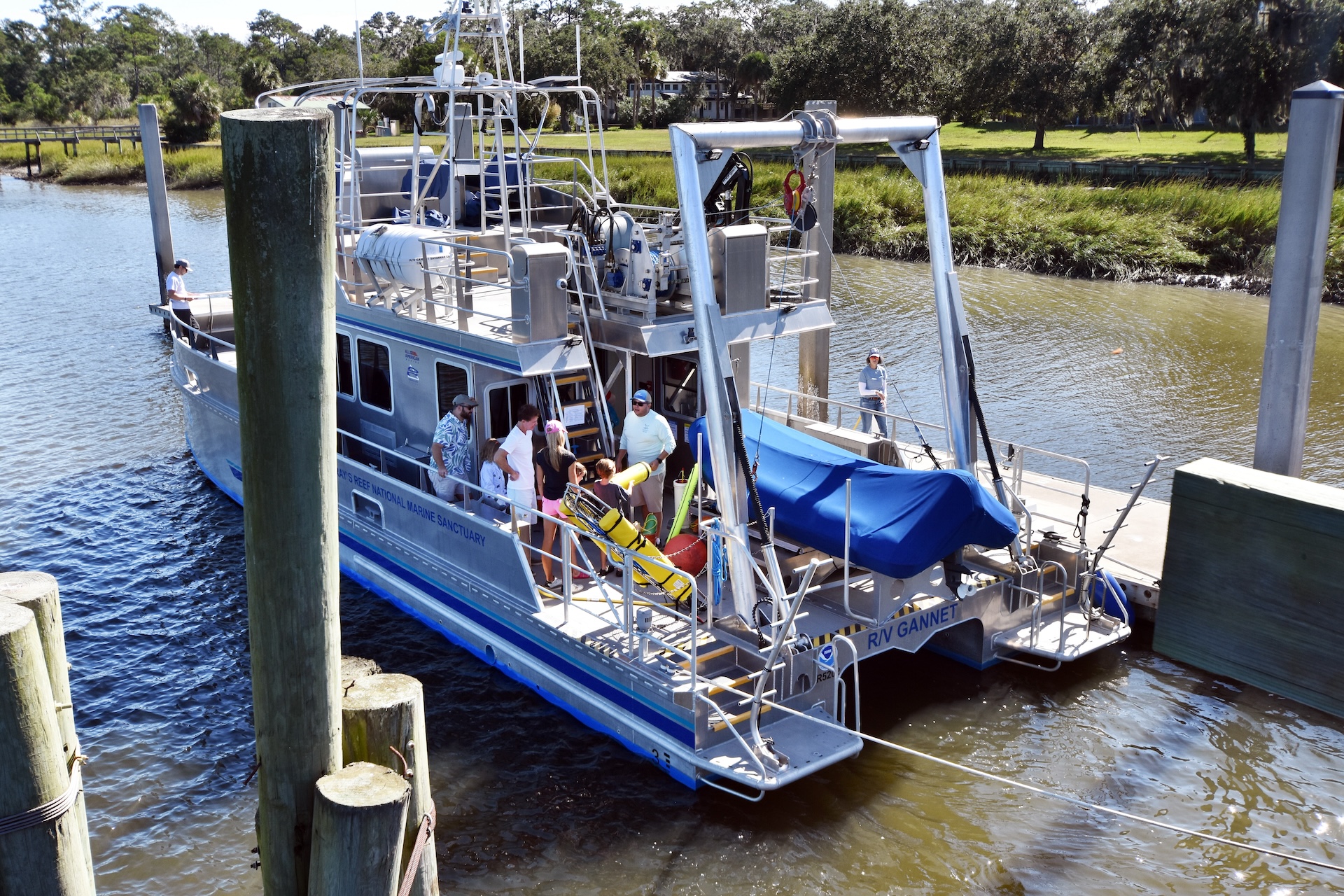 people stand on a large research vessel tied to a dock. 